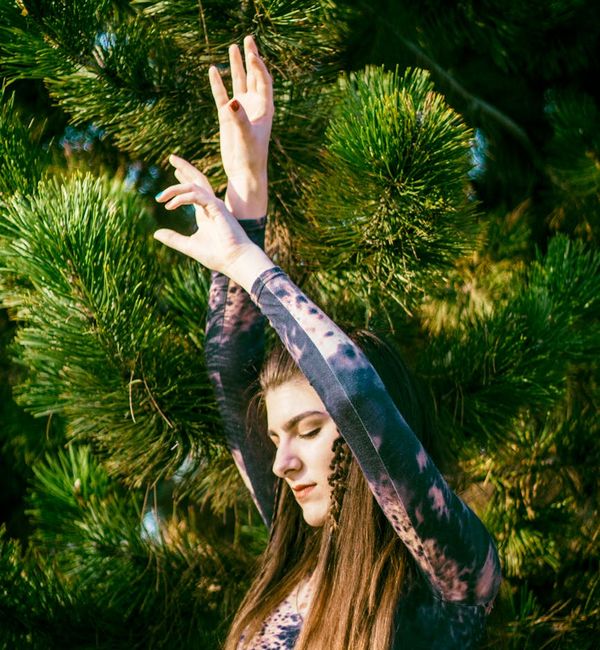 Woman in a graceful tree yoga pose against a pine green background.